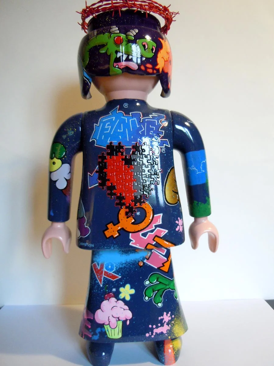 Playmobil bleu foncé et violet, graffé avec un coeur en puzzle dans le dos et une couronne en barbelé