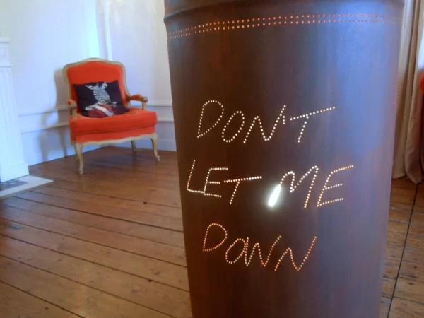 Photo du dos du bidon rouillé représentant un planisphère, on voit la phrase suivante "don't let me down" en lettres lumineuses.
