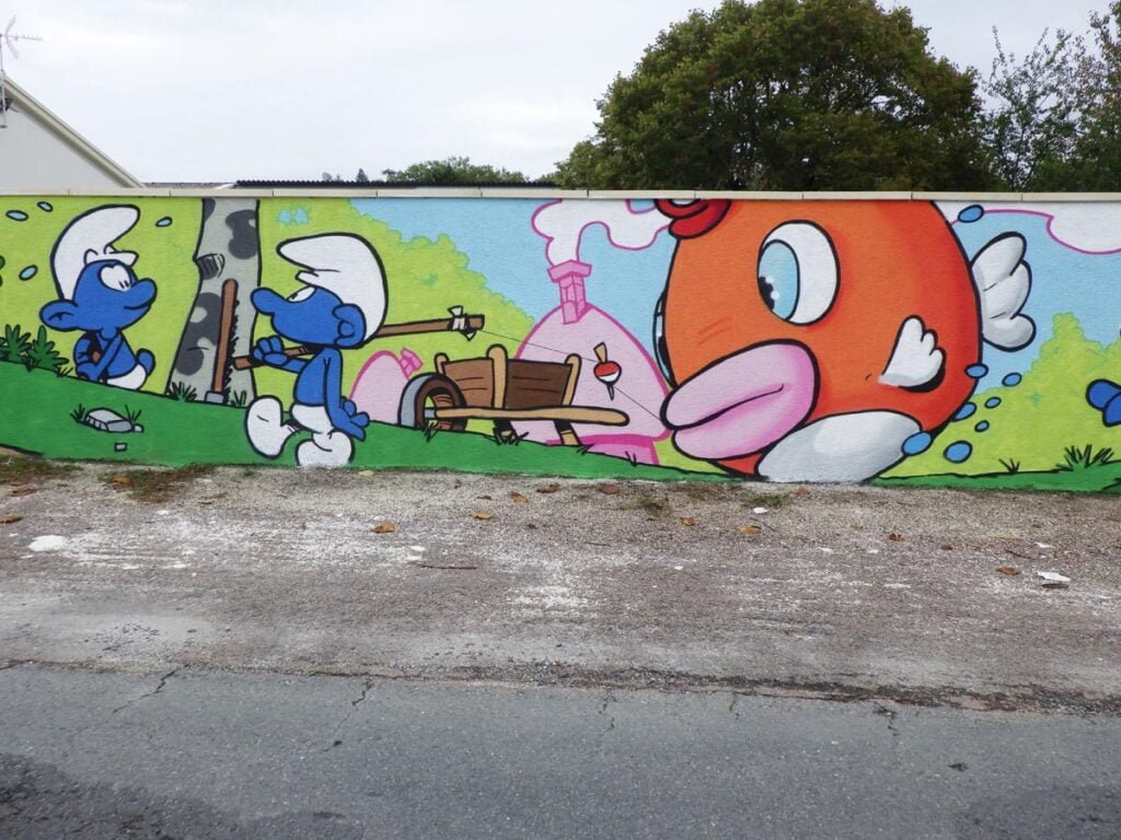 Photo de la fresque Schtroumpf montrant en plan serré un Schtroumpf qui revient de la pêche avec sa canne sur l'épaule et il traine un énorme poisson derrière lui. Le poisson est un Cheep Cheep, les poissons que l'on retrouve dans les jeux Mario Bros.