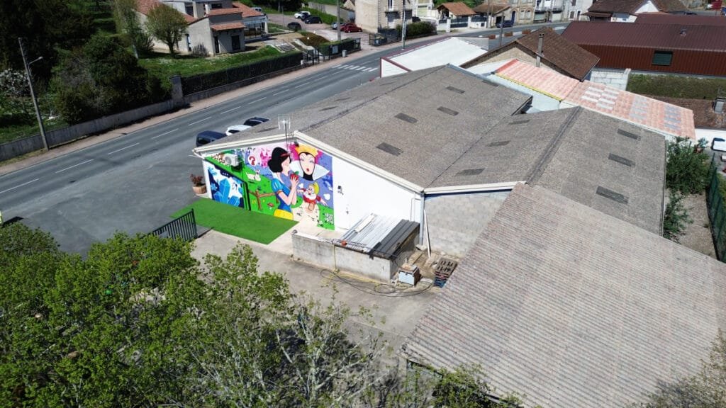 Photo aérienne de la fresque de Blanche Neige par drone. On voit une vue très large du bâtiment sur lequel la fresque est peinte. Fresque réalisée par Marcel Champion.