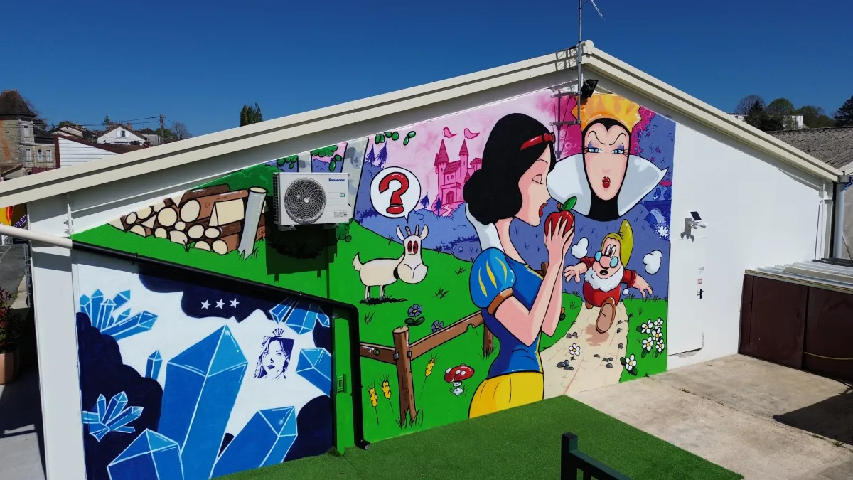 Photo de la fresque Blanche Neige vue de coté. On se rend bien compte que les couleurs qui composent cette réalisation sont éclatantes. On voit Blanche Neige tenant une pomme rouge dans sa main, un nain qui court vers elle pour la prévenir du danger et la Reine au second plan qui observe sans rien dire.