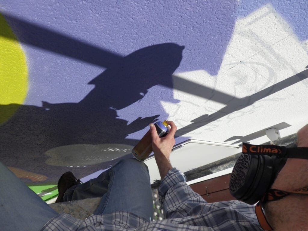 Photo de Marcel Champion en train de graffer. Il est installé sur un échafaudage et a les pieds dans le vide.