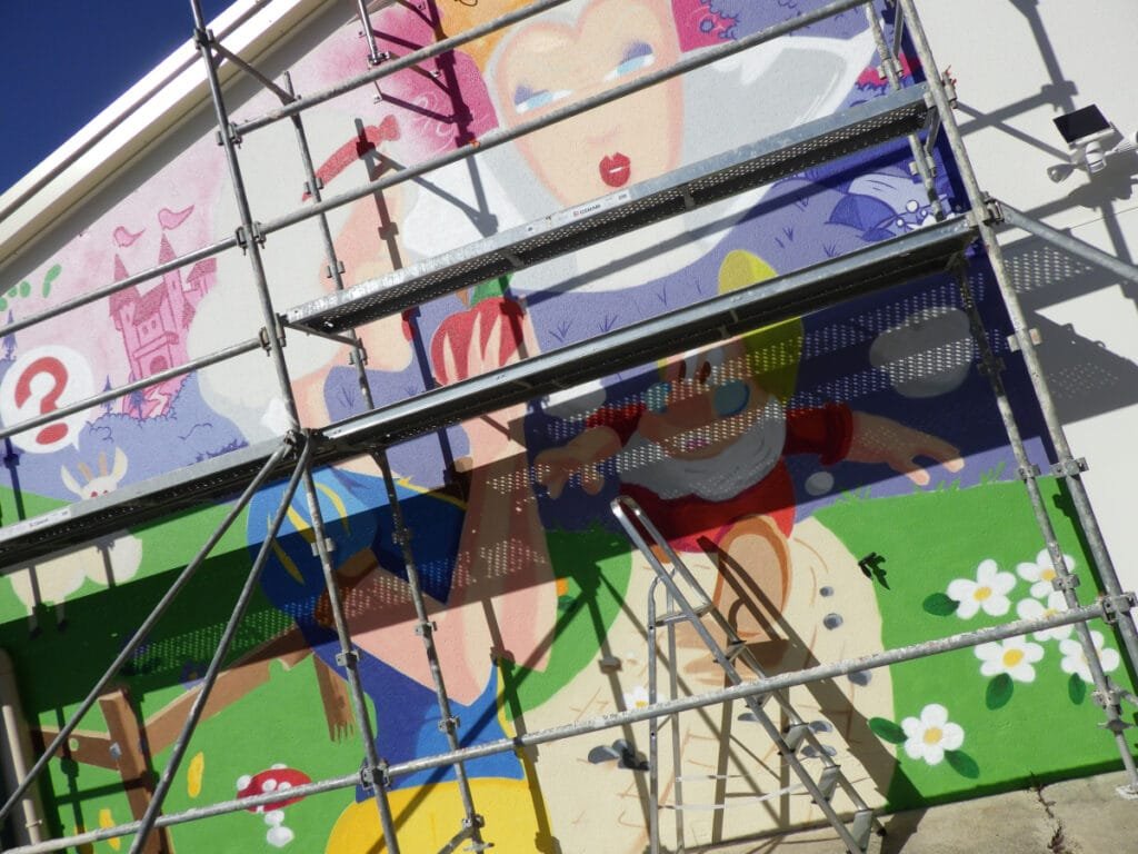 Photo de l'échafaudage utilisé pour réaliser la fresque Blanche Neige. On voit très nettement que le travail a bien avancé et que la plupart des couleurs sont déjà en place sur la mur.