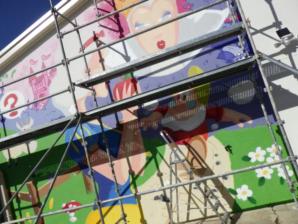 Photo de l'échafaudage utilisé pour réaliser la fresque Blanche Neige. On voit très nettement que le travail a bien avancé et que la plupart des couleurs sont déjà en place sur la mur.