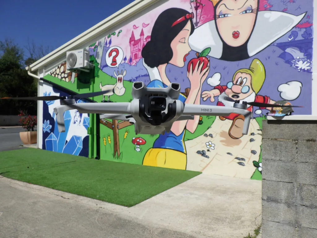 Photo du drone stationné devant la fresque Blanche Neige. Le drone DJI fait nous fait face et semble nous regarder.