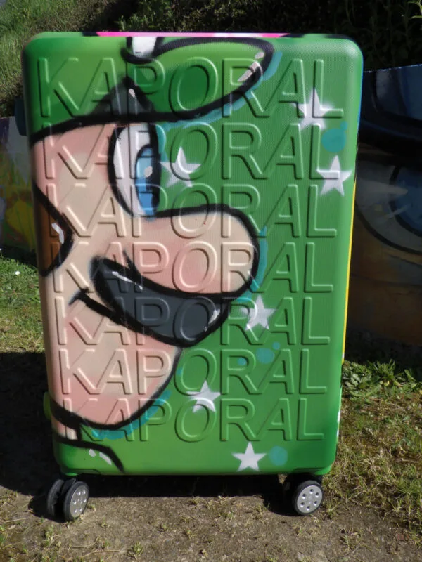Photo du coté de la valise à roulette graffé aux couleurs de mario bros et Luigi. Sur cette photo on voit la coté avec la tête de Luigi. Une belle façon de voyager avec style.