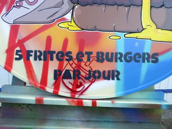 Gros plan sur le texte présent en bas du tableau. Il est inscrit : "5 frites et burgers par jour" en gris anthracite. Cette couleur permet une très bonne lisibilité car le contraste avec le fond clair et chaud est fort.