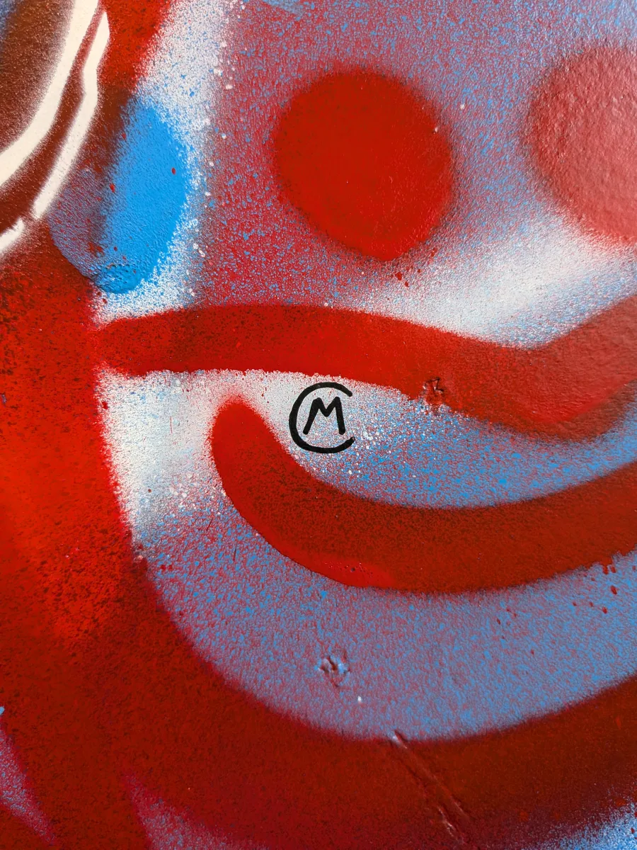 Plan serré sur la signature de Marcel Champion. Avec au second plan les détails de la partie graffée du tableau. On distingue bien les goutellettes de peinture, typique des peintures en bombe.