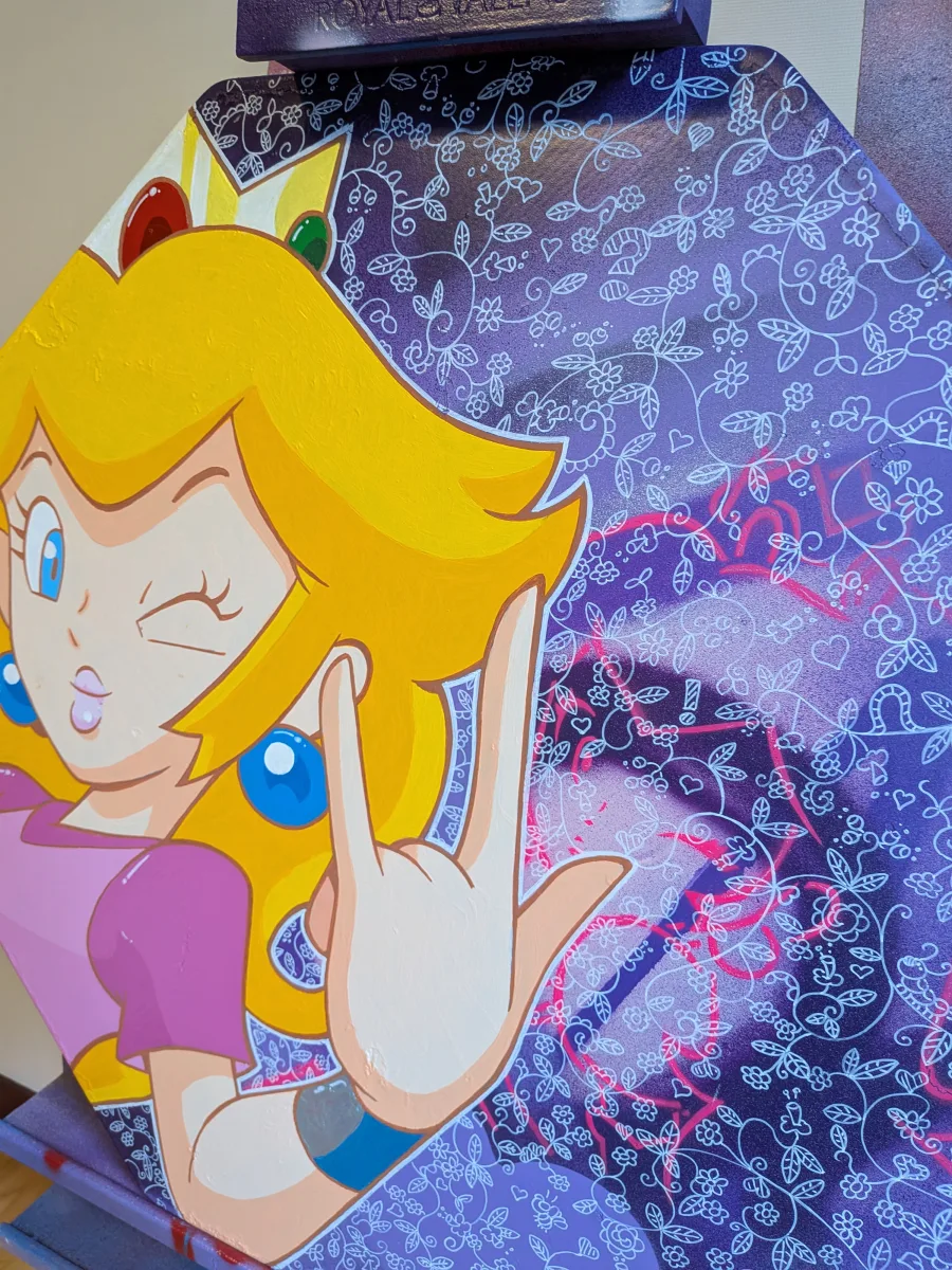 Gros plan sur cette œuvre 100 % artisanale réalisée sur un vrai panneau de signalisation routière octogonal en métal (format STOP 60 cm). Princesse Peach ultra-charismatique : clin d’œil provoc’, langue tirée et main en cornes rock, sur un fond violet intense recouvert d’une superbe dentelle florale blanche ultra-fine réalisée au posca et bombe. Touches de spray rose fluo viennent dynamiter ce décor romantique. Pièce unique street-pop qui mixe univers Nintendo, attitude punk et élégance victorienne. Mots-clés : Princesse Peach peinture, panneau stop customisé, street art Nintendo, tableau gaming dentelle, Peach rock, décoration geek chic, pop art Mario, œuvre originale panneau routier, cadeau gamer. Support aluminium d’origine, finitions premium, prête à accrocher !