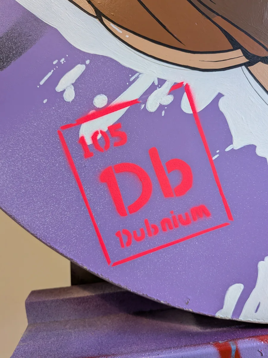 Détail audacieux sur l’œuvre pop-art ronde : la pastille de l’élément 105 DUBNIUM (Db) est peinte en rouge fluo vif au pochoir, avec légers débordements et éclaboussures blanches qui rappellent la nature ultra-rare, radioactive et synthétique de cet élément transactinide découvert en 1968-1970 à Dubna (Russie). Symbole Db surdimensionné, typographie inversée et texture brillante : clin d’œil geek parfait entre chimie extrême et street art contemporain. dubnium Db 105 street art, élément 105 tableau périodique pop art, dubnium radioactif peinture urbaine, pochoir rouge fluo Db détail, œuvre signalétique dubnium Russie 2025, art contemporain élément transactinide
