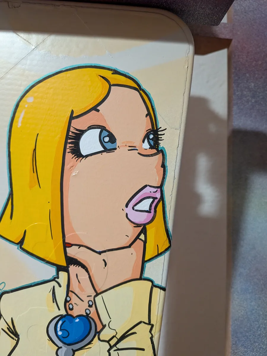 photo montrant en gros plan le visage de Circé Love peint sur un panneau signalétique. Elle porte un médaillon bleu en forme de coeur.