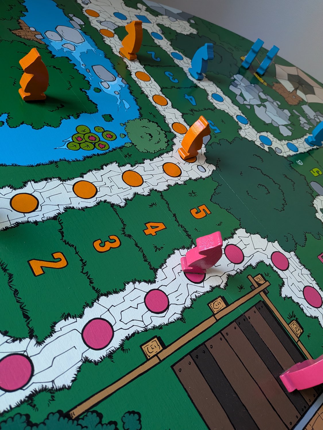 vue en plan serré du plateau de jeu peint sur une table ronde. On découvre les détails peints à la main d'un jeu de petits chevaux avec des pièces en bois aux couleurs des emplacements.